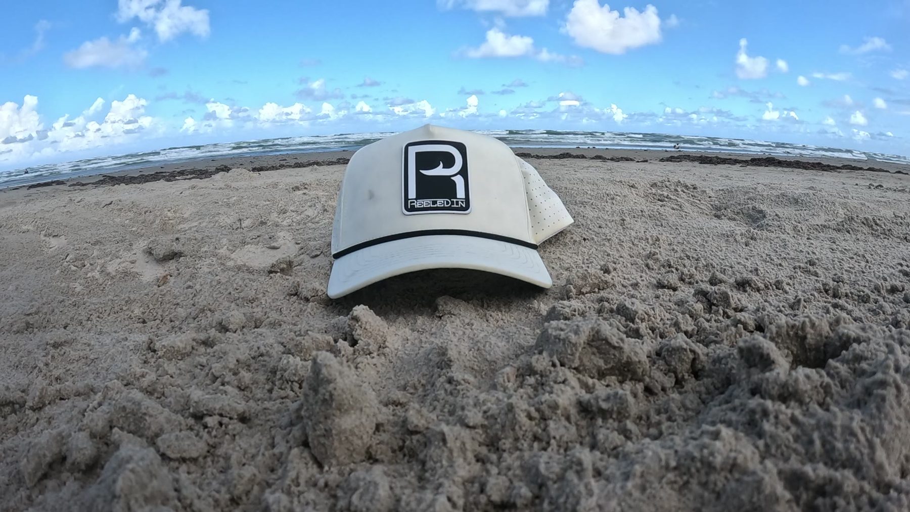 White Reeled In rope hat sitting in the sand, the surf behind