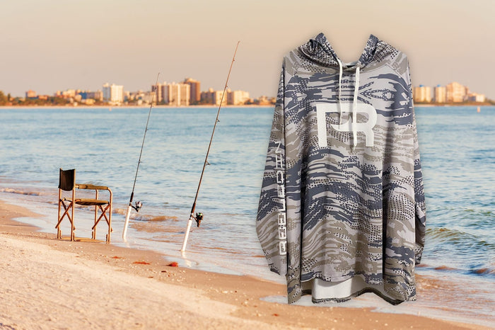 Reeled In performance hoodie hanging on the beach beside rods