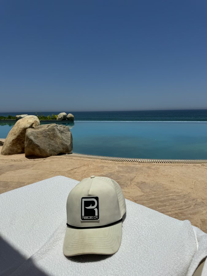 Reeled In hat on the rocks at the water's edge